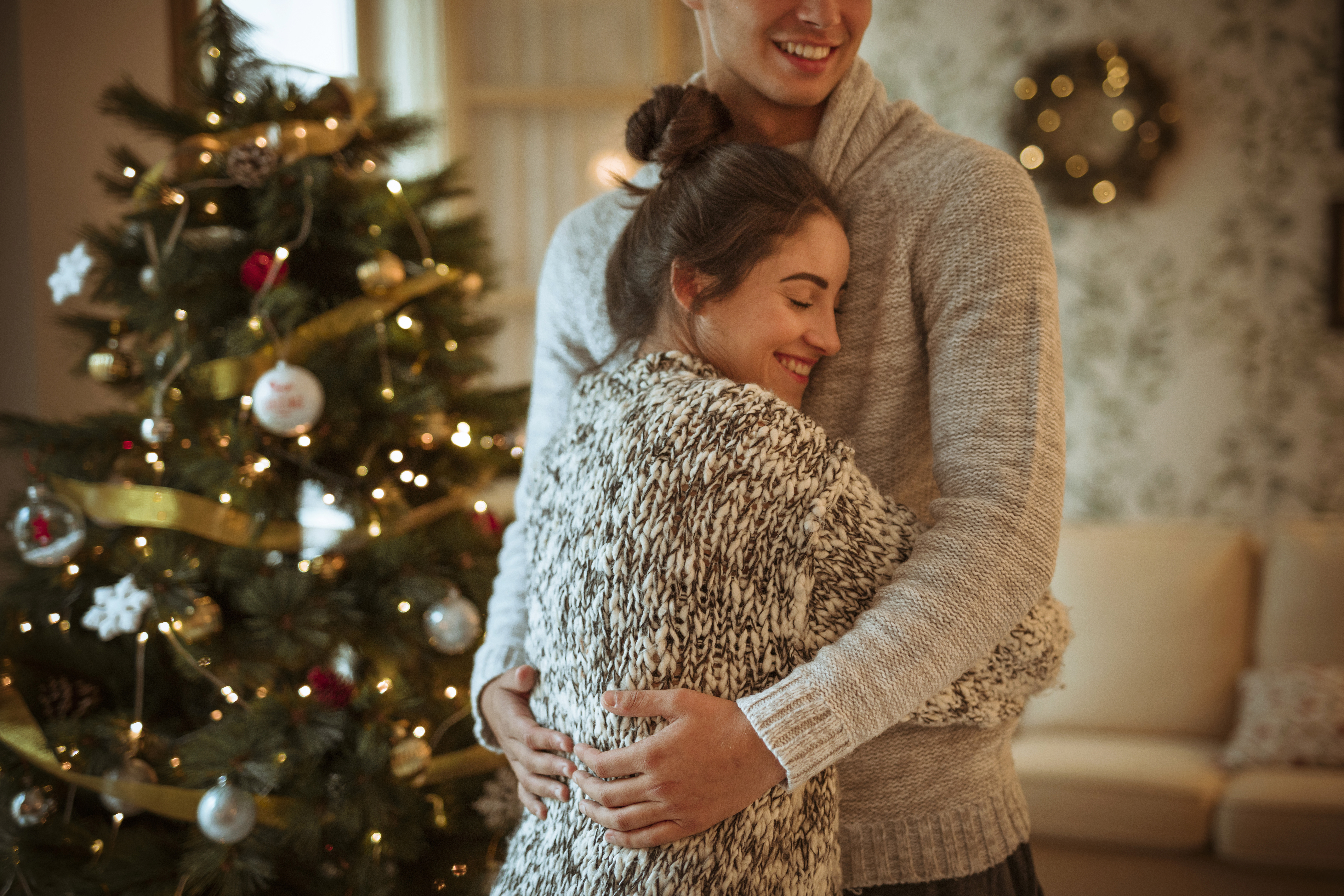 young-woman-hugging-man-near-decorated-fir-tree