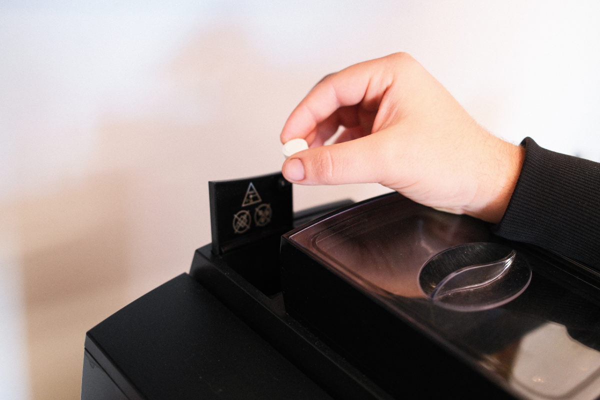Ruka vkládá čistící tabletu do automatického kávovaru během pravidelné měsíční údržby