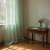 Soft mint green, textured curtains billowing slightly inward from an open window, sheer sunlight streaming through the fabric creating lumi