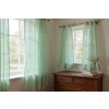 A cozy, sun drenched bedroom scene featuring light, airy mint green linen curtains gently billowing in the breeze from an open window The room is bathed in