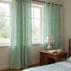 Sun drenched bedroom featuring floor to ceiling, soft, seafoam green linen curtains billowing gently in the breeze from an open window, casting diffused li
