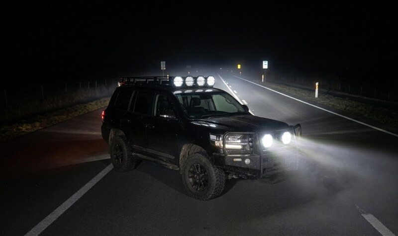 Detailní čelní pohled na rozsvícené přídavné dálkové LED světlo s duálním pozičním světlem v dálkovém režimu. Jasně bílé světlo se odráží v členité optice a podtrhuje robustní konstrukci světlometu. - Přídavné dálkové LED světlo s duálním pozičním světlem, 144W, 13000Lm, IP69K, R149, R148