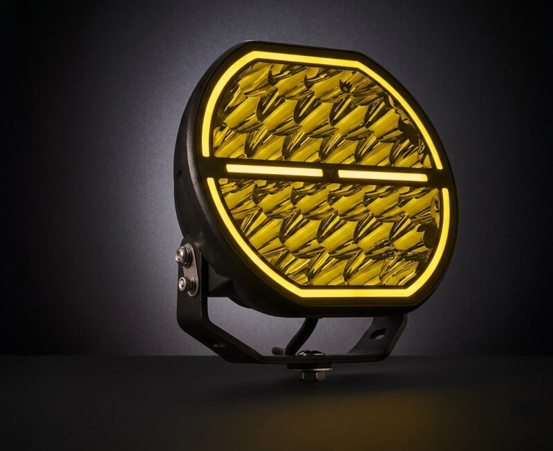 Detailní makro pohled na čočku přídavného dálkového LED světla s duálním pozičním světlem. Je aktivován duální režim a obvodový kroužek svítí sytou žlutou barvou, která ostře kontrastuje s tmavým vnitřkem světlometu. - Přídavné dálkové LED světlo s duálním pozičním světlem, 164W, 15000Lm, IP69K, R10, R148, R110