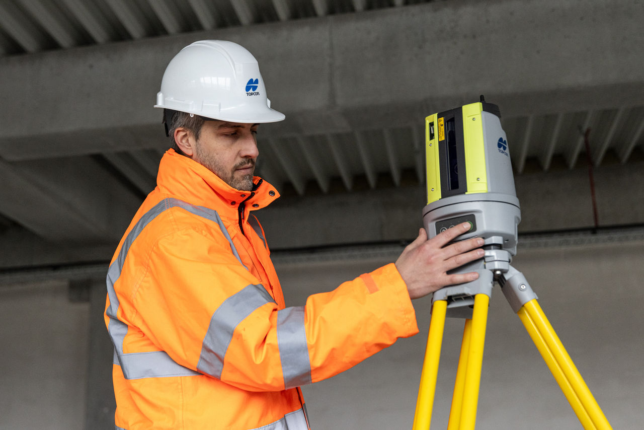 Technik v reflexní bundě a přilbě staví vytyčovací systém Topcon LN-50 na stativ na stavbě