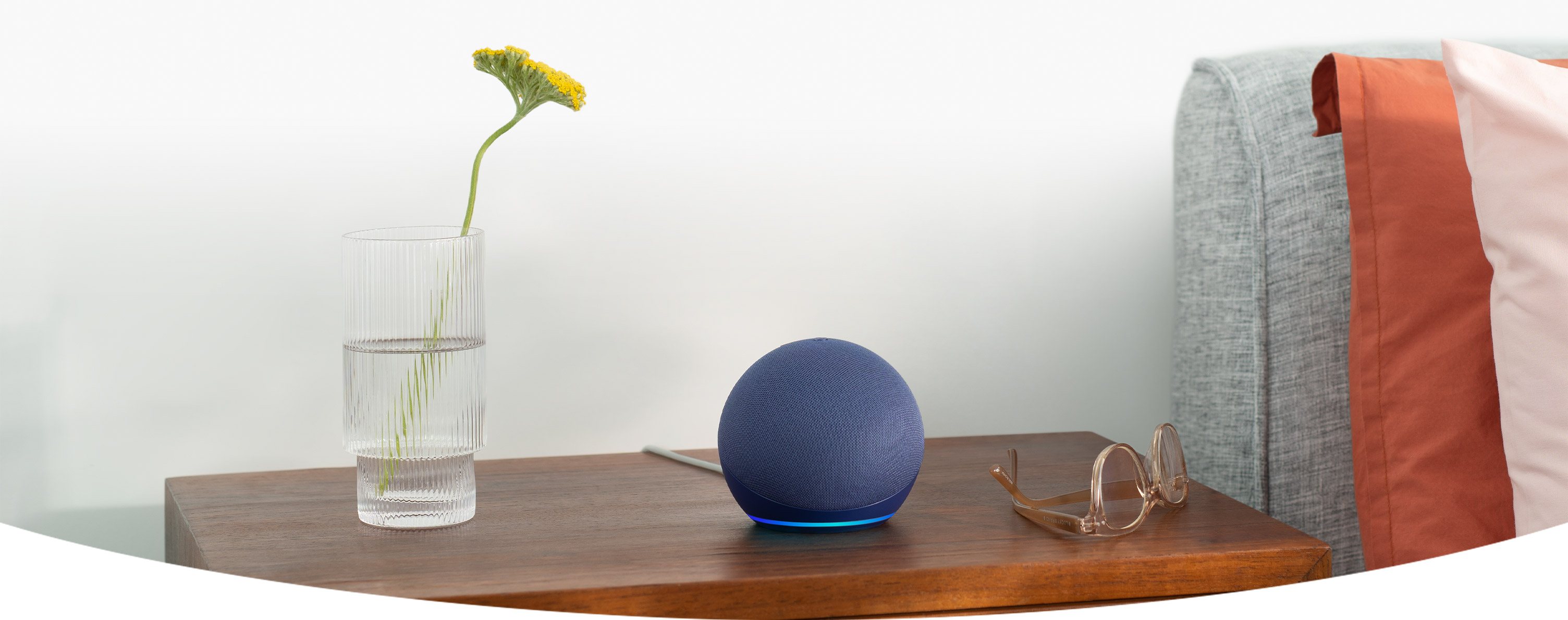 Modrý Amazon Echo Dot na nočním stolku vedle vázy a brýlí