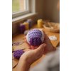 Close up shot of a handcrafted, multi toned purple crochet ball, resting gently within the cupped hands of a young artisan; warm, diffuse natural light streams in through a nearby window, illuminating the intricate