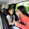 Autosedačka Joie Fortifi™ R129 nainštalovaná v aute - sedí v nej dievča a mama ju púta 3-bodovými pásmi