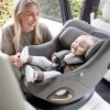 Autosedačka Joie i-Harbour™ E Signature v tmavošedej farbe ebony nainštalovaná v aute v protismere jazdy s dieťaťom a mamička ho púta