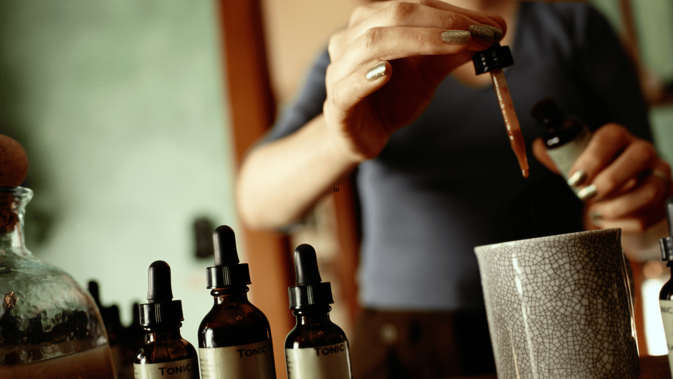 „Ruka držící kapátko nad skleněnou lahvičkou – rituál tinktur Alchemix v přírodním světle“