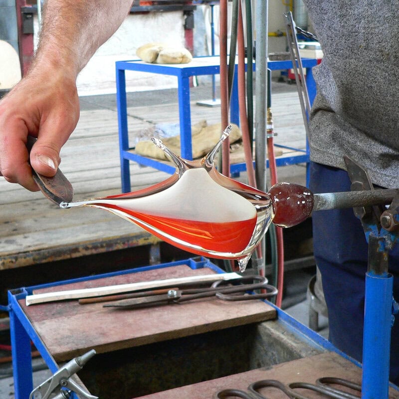 Ein Glasmacher formt von Hand eine Glasfigur in Form eines Fisches.