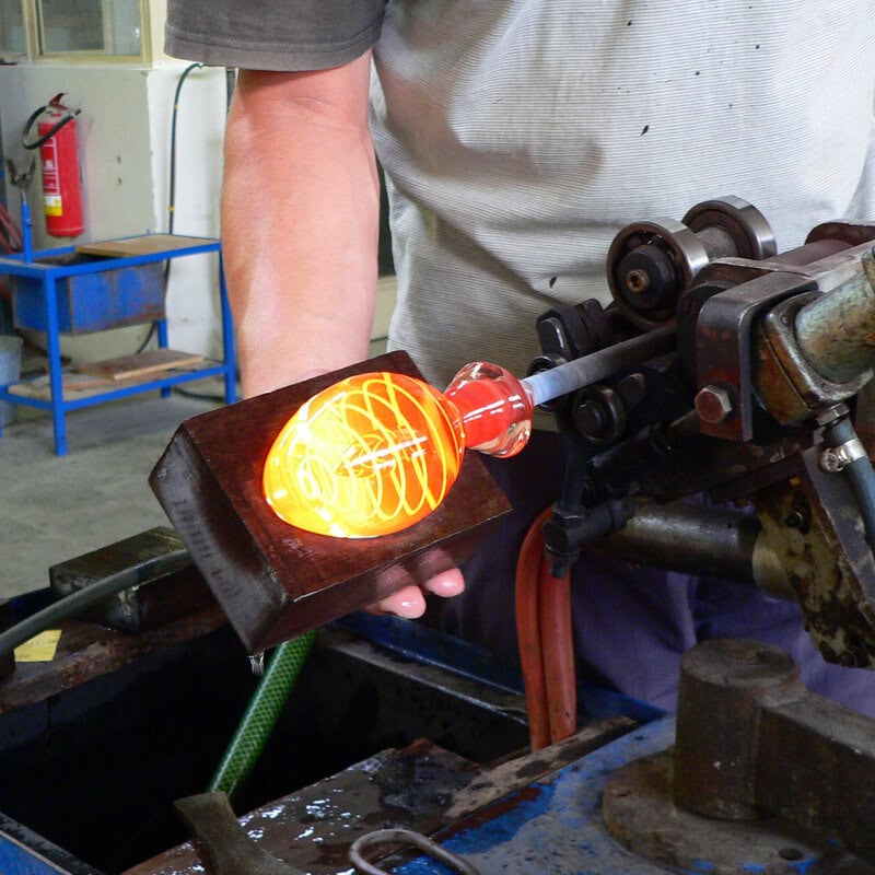 Ein Glasmacher formt ein glühendes, orange-gelbes Ei aus Glas.