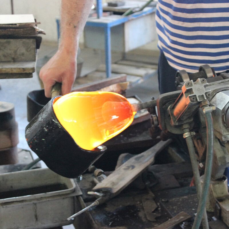 Close-up of a master glassblower shaping a glowing hot piece of glass at the furnace