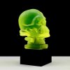 Side profile of Art Deco skull hood ornament in uranium glass on black glass base under UV light