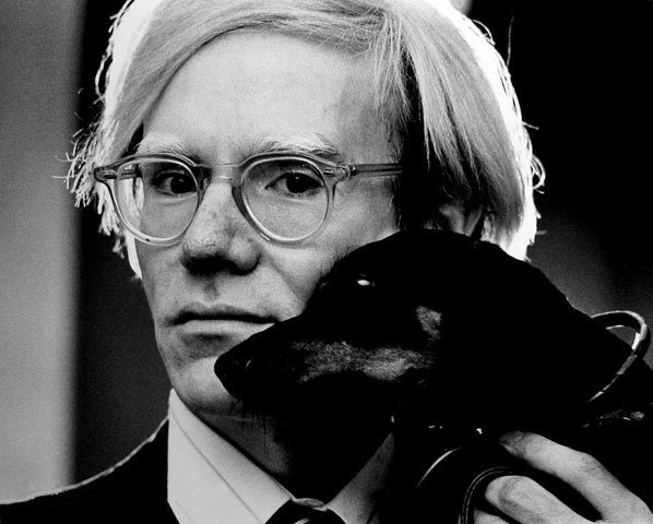 Andy Warhol v roce 1973 – černobílá fotografie muže se světlými vlasy, který drží v náručí jezevčíka