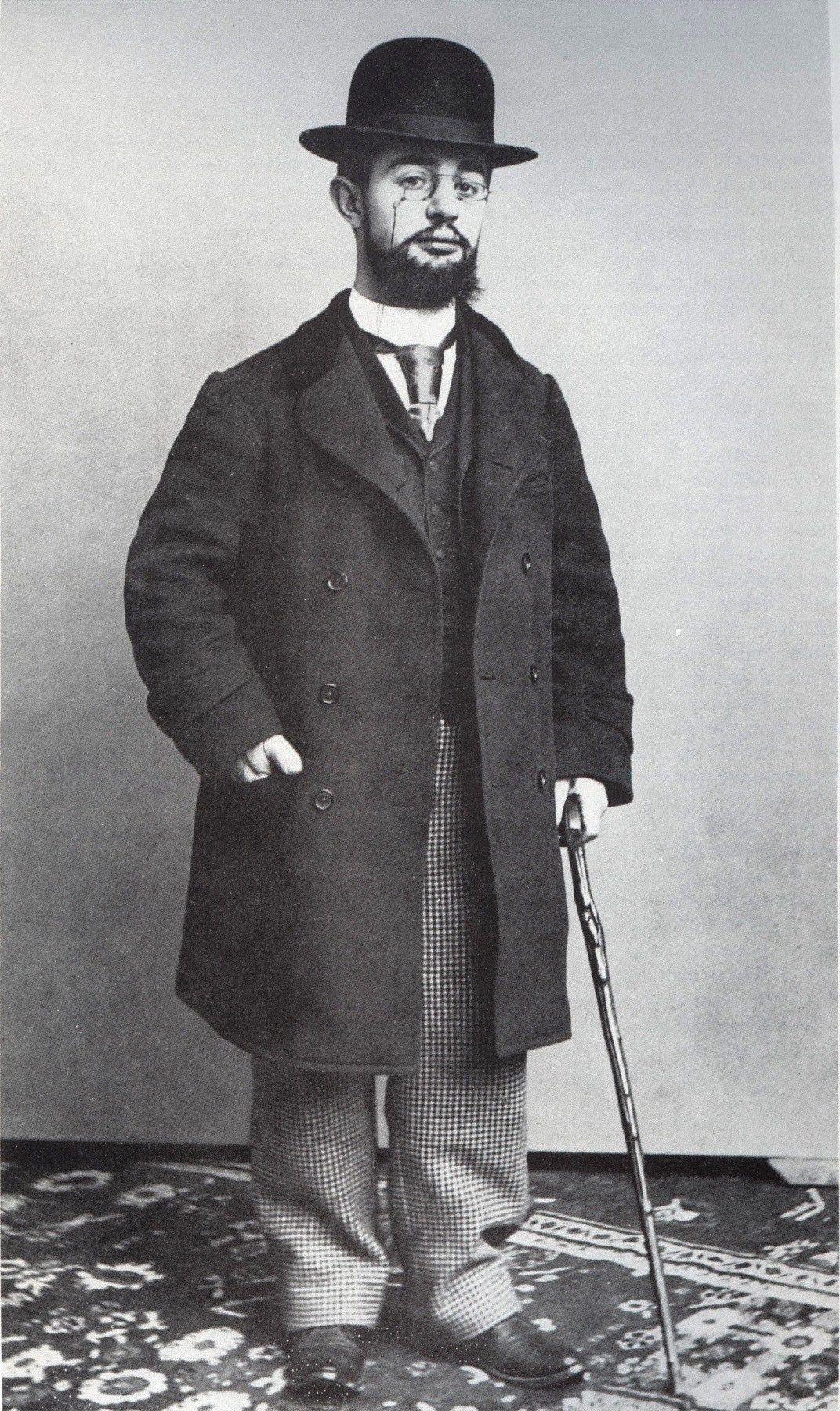 Henri de Toulouse-Lautrec v roce 1894 – černobílá fotografie muže s buřinkou, plnovousem, v dlouhém kabátě a s vycházkovou holí