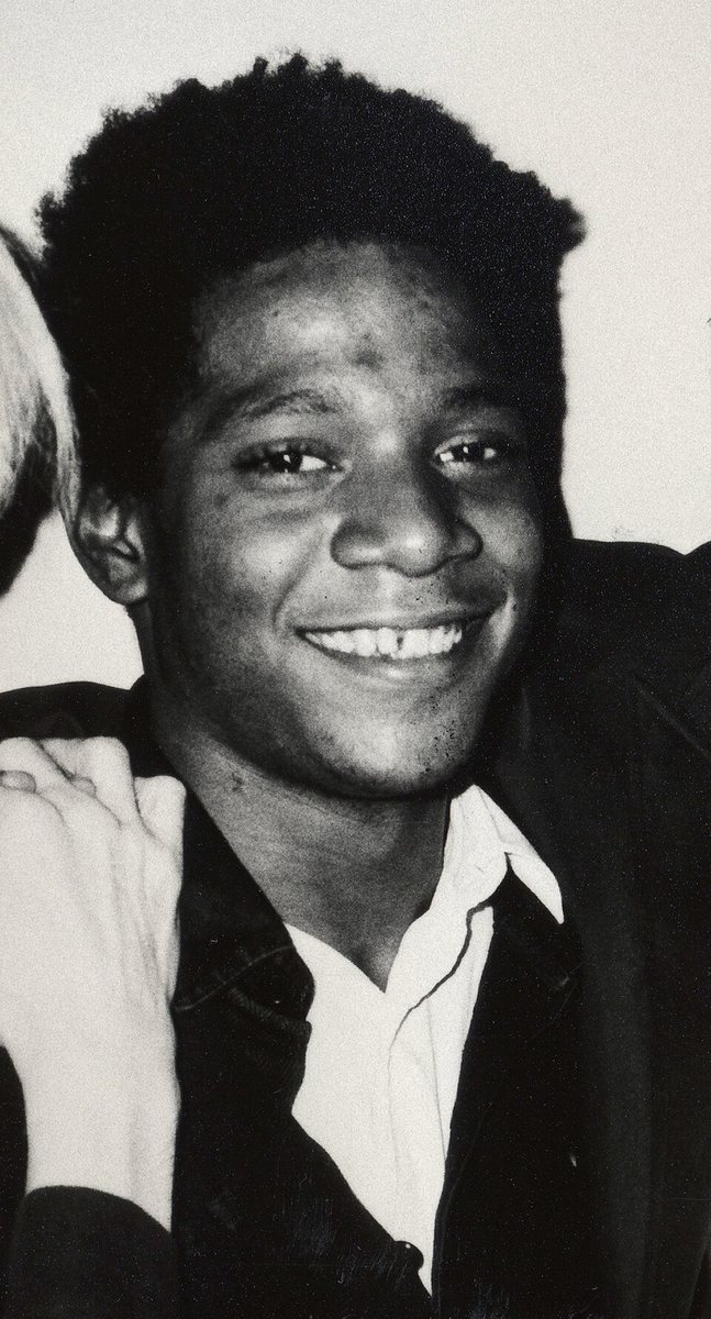 Jean-Michel Basquiat v roce 1984 – černobílá fotografie usměvavého mladého muže v tmavém saku a bílé košili