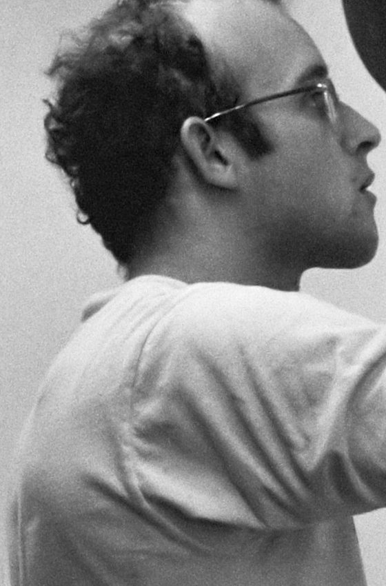 Keith Haring v roce 1986 – černobílá fotografie mladého muže s kudrnatými vlasy a brýlemi z profilu