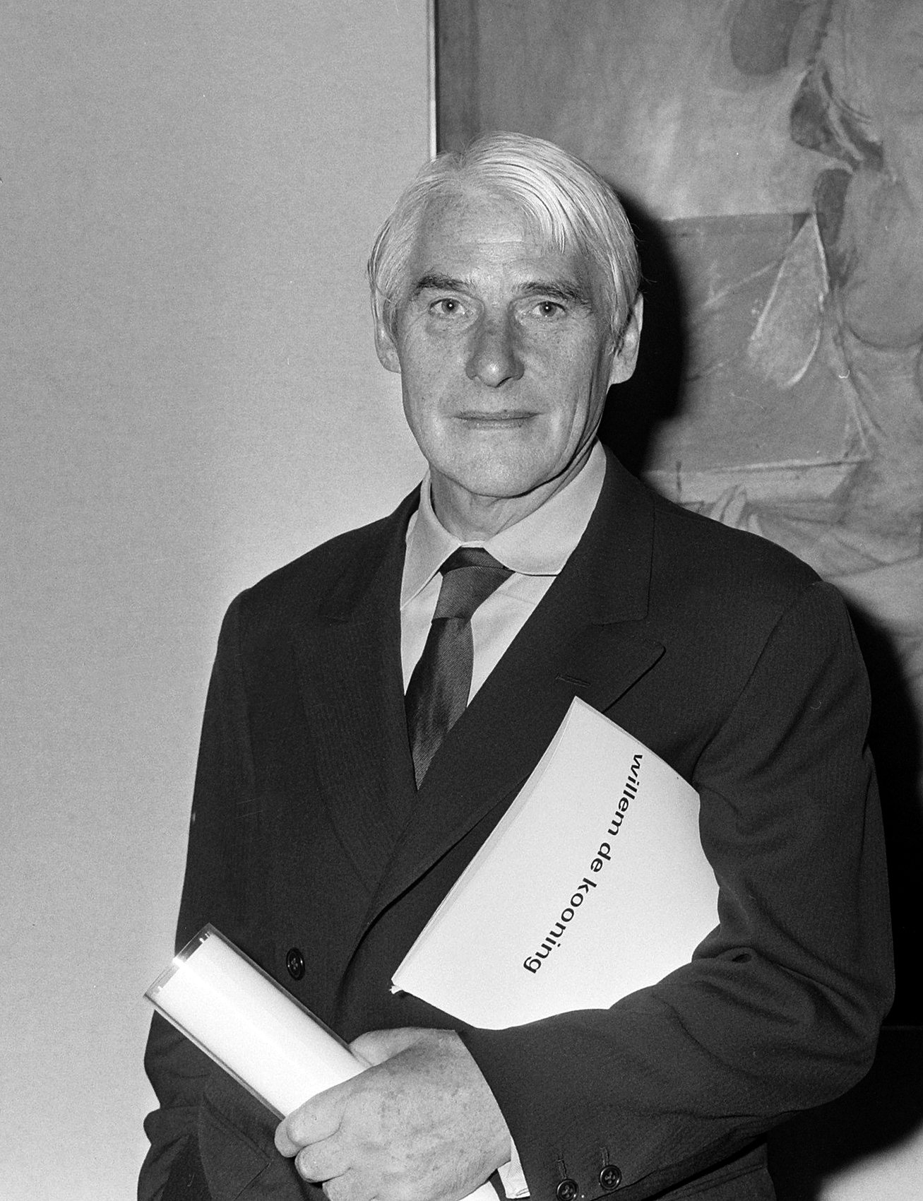 Willem de Kooning na fotografii z roku 1968 – starší muž s šedivými vlasy v saku a kravatě drží v ruce papíry