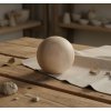 28505 5 drevena dekorace koule 15cm z hladkeho svetleho dreva polozena na bezovem platne a rustikalnim drevenem stole s hlinenymi a prirodnimi dekoracemi v rozostrenem pozadi