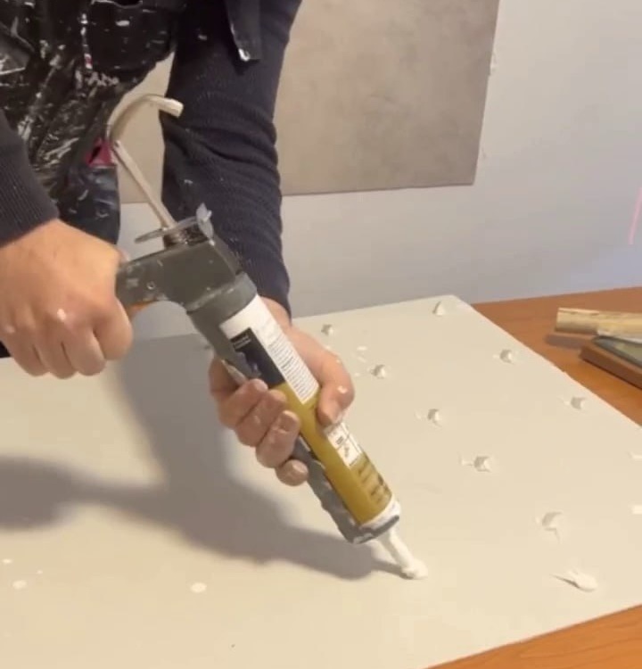 Aplikácia montážneho lepidla na zadnú stranu PVC panelu pred montážou