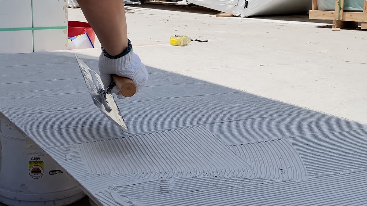 Nanášanie cementového lepidla na zadnú stranu flexibilného kamenného panelu 120 × 300 cm pomocou zubovej stierky pred lepením na stenu