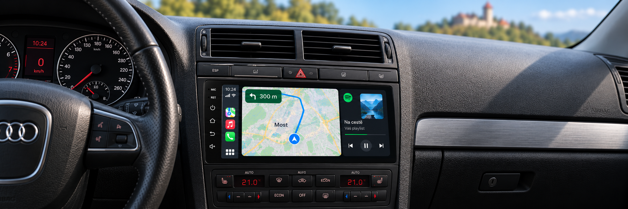 CarPlay s navigací Most v interiéru Audi A4 a rozmazaným Hněvínem v pozadí