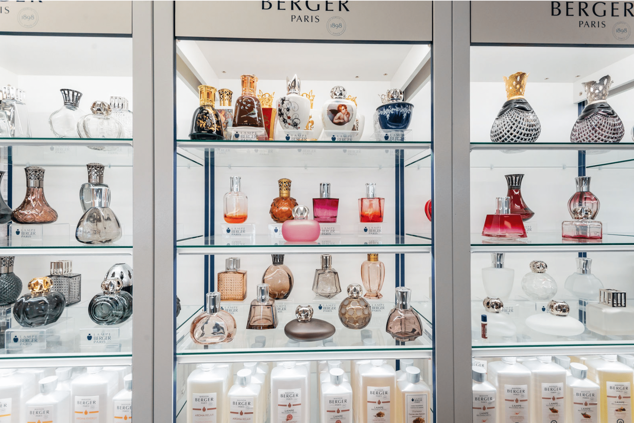 Pestrá vitrína s designovými katalytickými lampami Maison Berger Paris různých tvarů a barev