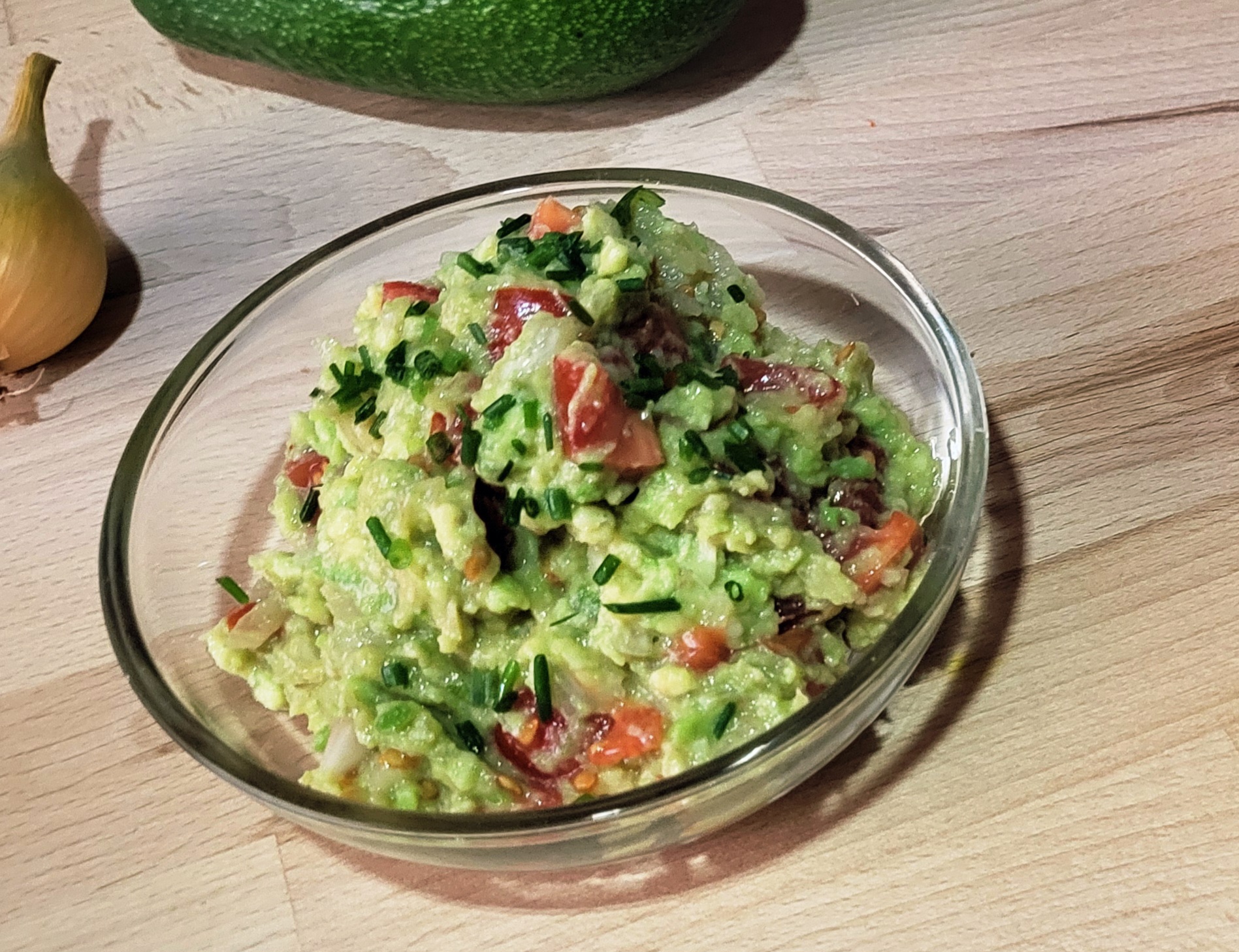avokadova pomazanka guacamole s rajcaty a cibuli v misce na drevenem stole