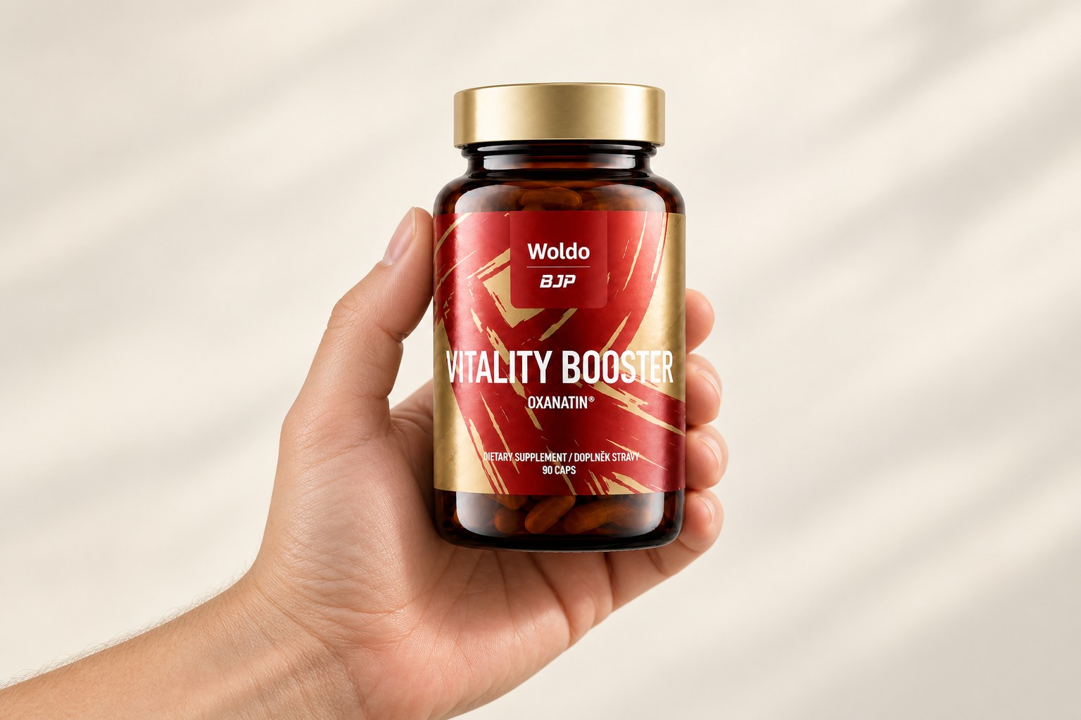 Ruka držící jantarovou dózu Vitality Booster s červeno-zlatou etiketou na světlém pozadí