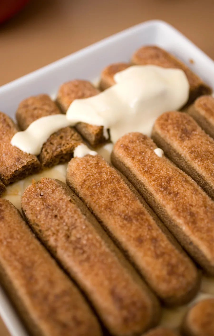 Vrstvenie tiramisu — savoiardi piškóty namočené v espresse a mascarpone krém vo forme