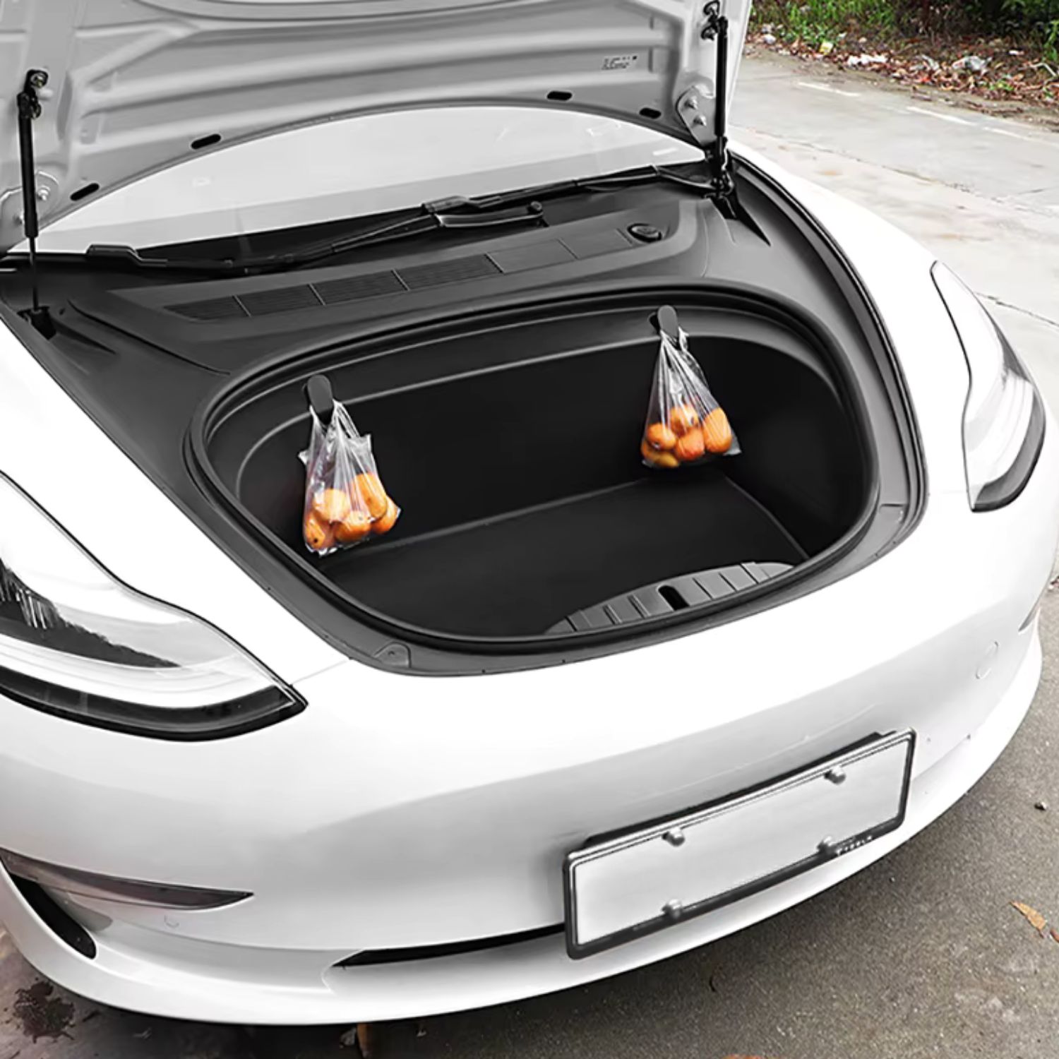 Bílá Tesla z dálky s otevřeným předním kufrem, kde háčky perfektně drží nákupní tašky
