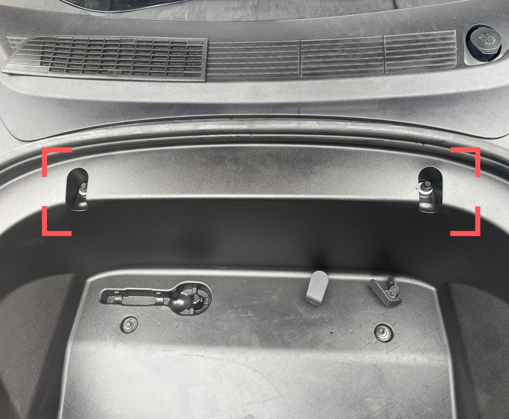 Pohled do předního kufru Tesly Model 3 před instalací - pouze plochá plastová krytka šroubu