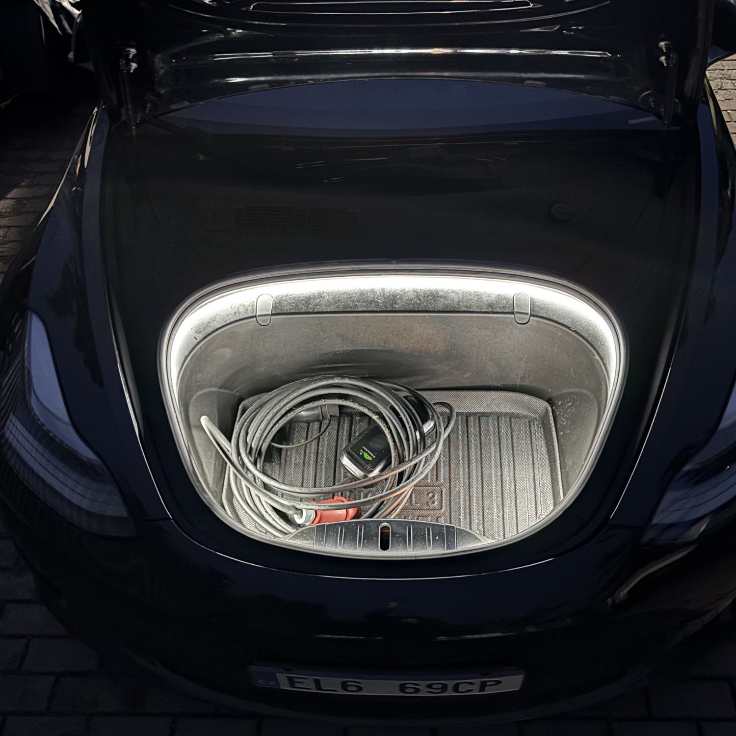 Pohled na přední kufr Tesla Model 3 otevřený v noci, osvětleno LED páskem