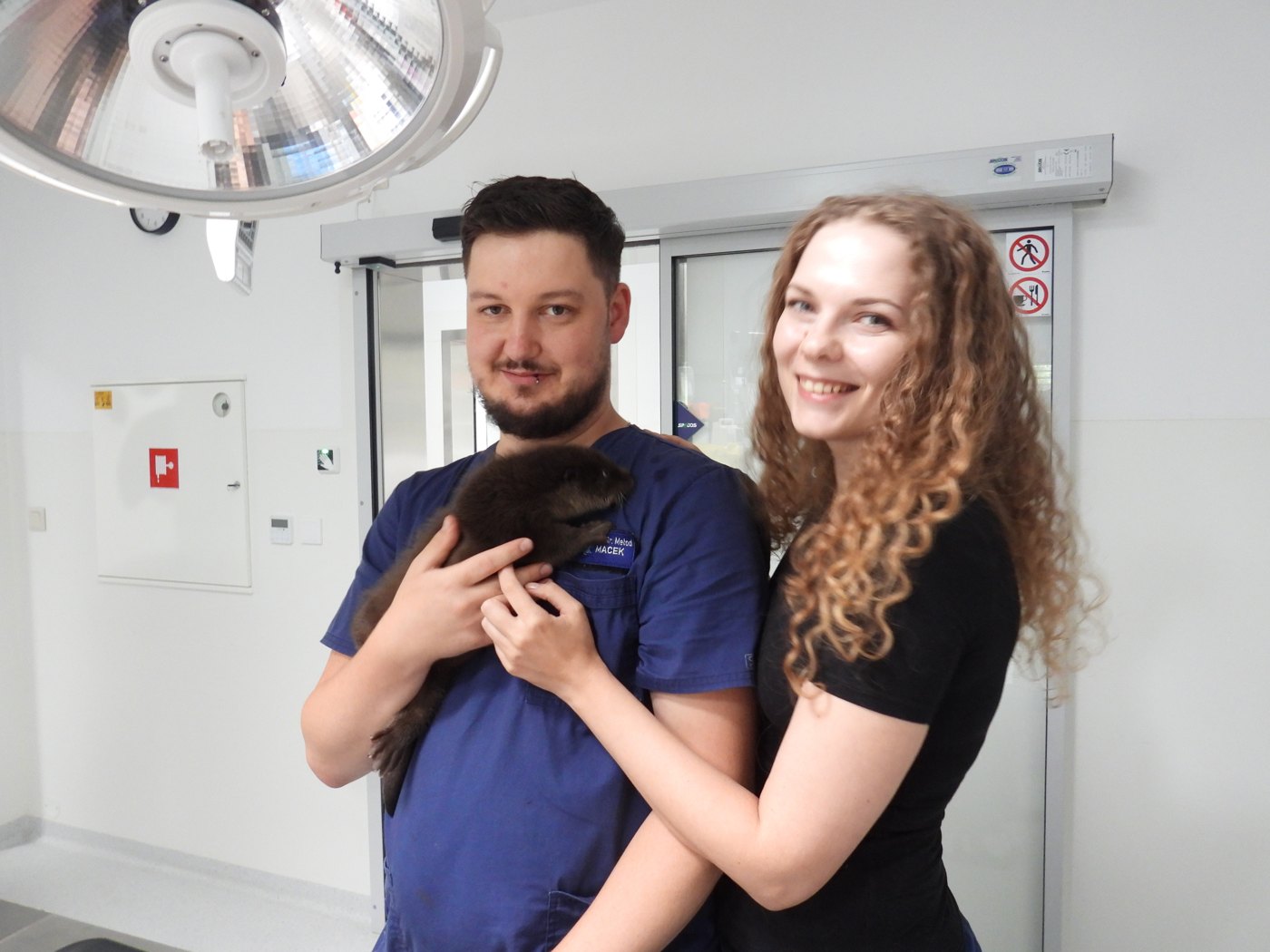Muž v modrom veterinárnom oblečení a žena držia tmavé mláďa