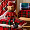 Vianočný medvedík v červenom kabáte sediaci na károvanej prikrývke – sviatočná dekorácia do obývačky alebo na stôl