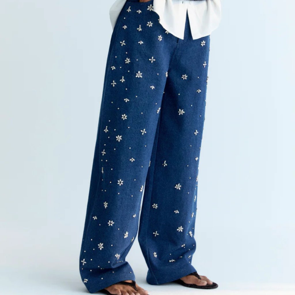 A stylish wide-leg denim pant featuring delicate hand-applied crystal details on the front for a subtle touch of sparkle. Designed with patch pockets at the back and finished with TNS embroidery on the waistband, it combines casual comfort with refined, unique details.  Model: Height 176 cm. Is wearing size S  Made in India  Color Collection: Blue Denim  100% Cotton