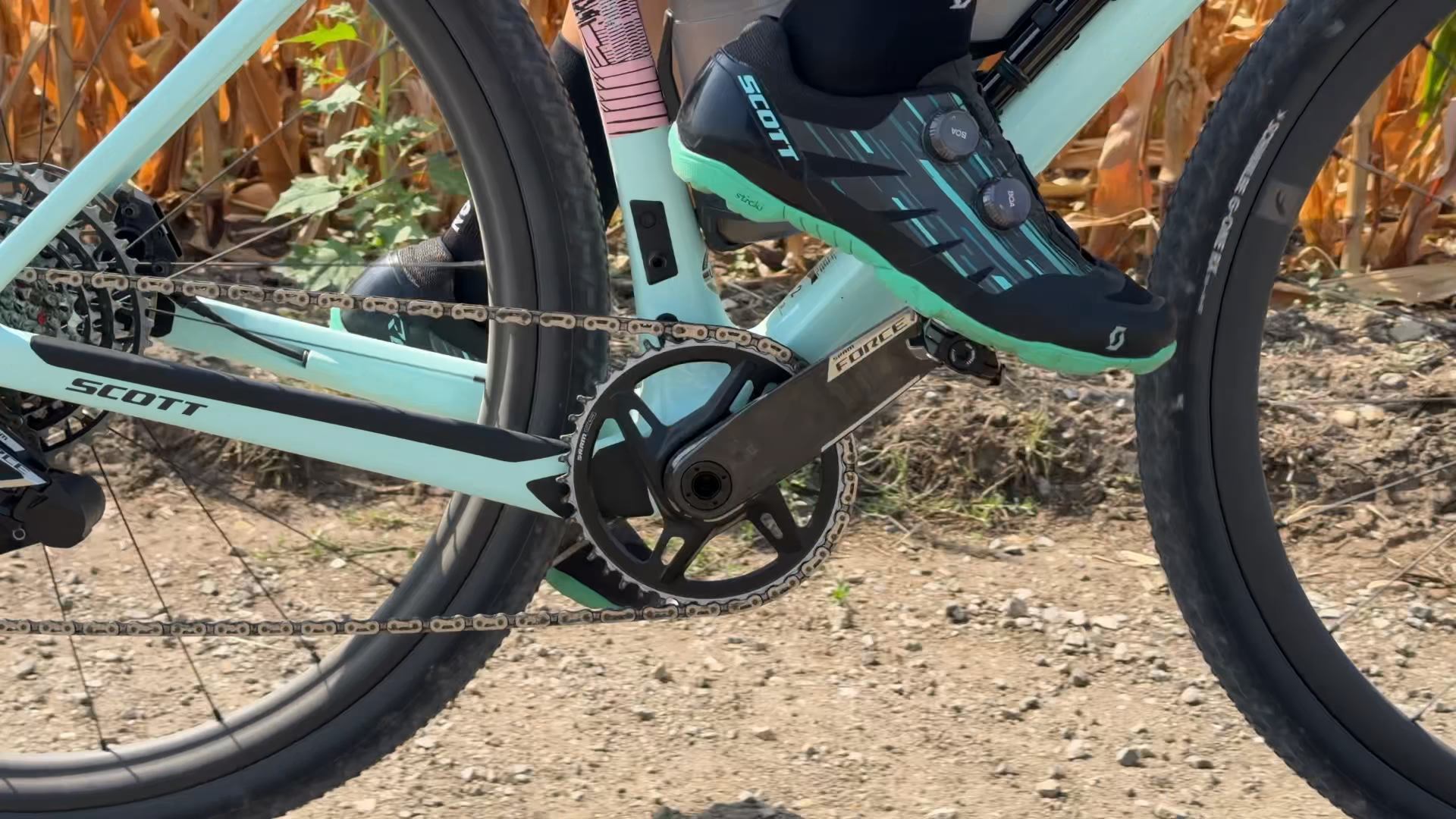 Detail pohonu na mätovom bicykli Scott: karbónová kľuka s jedným prevodníkom, reťaz a tretra Scott pri šliapaní po poľnej ceste.