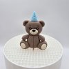 Roztomilá figúrka hnedého medvedíka s modrou bodkovanou čiapočkou, ideálna dekorácia na oslavu pre chlapca.