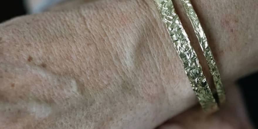 Detailní pohled na texturované zlaté náramky na ruce.