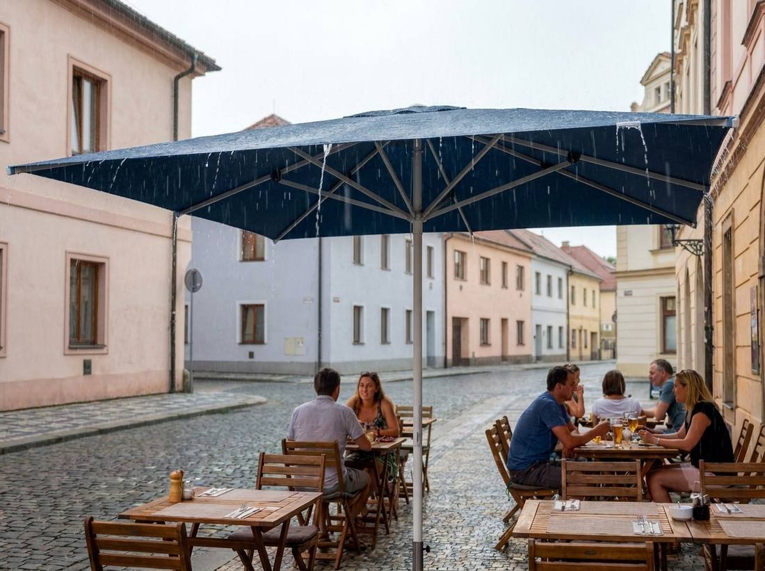 Voda stékající ze střechy modrého slunečníku Alu-Expert za deště, hosté sedí v suchu pod ním