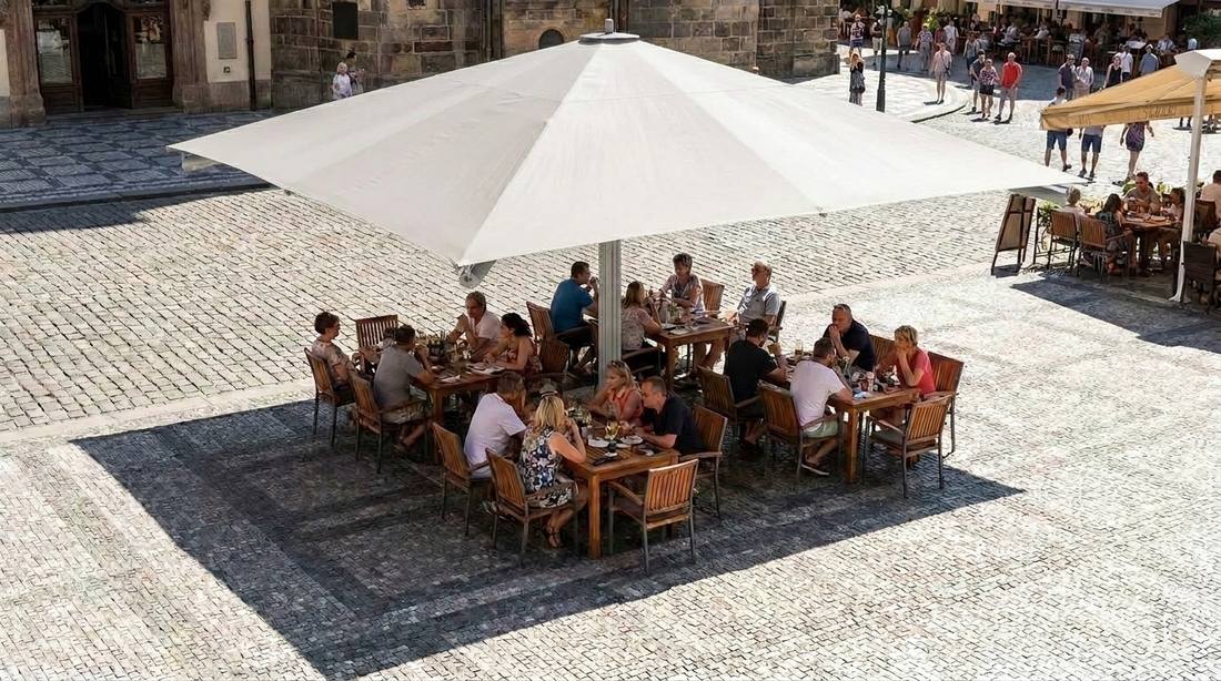Pohled shora na slunečník Goliath 400 x 400 cm v bílé barvě zastiňující několik obsazených stolů