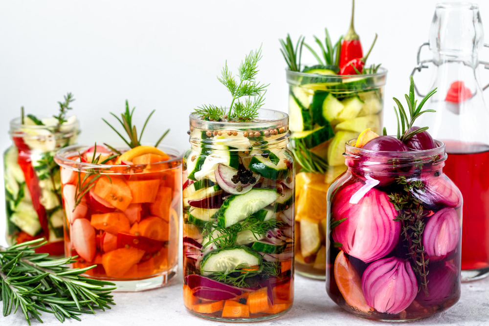 Sklenice s fermentovanou zeleninou – okurky, mrkev, cibule a bylinky jako přírodní zdroj vitaminu K2.