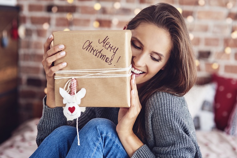 cheerful-woman-sitting-on-bed-and-holding-a-gift-SLWTFJX