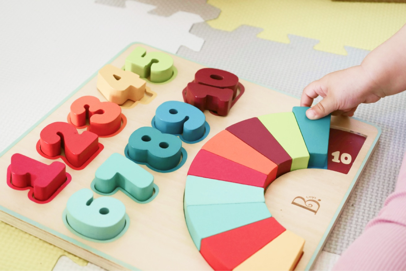 Dětská ruka skládá barevné dřevěné puzzle s čísly