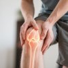 A european person gently holding their knee, with a glowing overlay highlighting the joint. The imag...