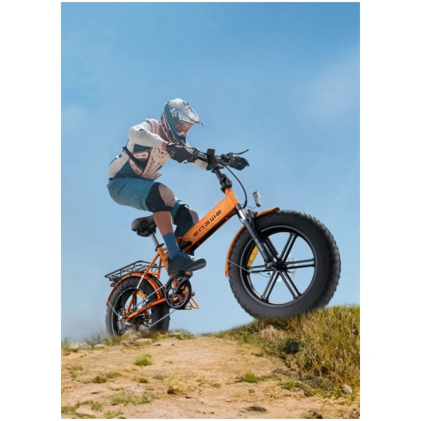 Na obrázku je zobrazen cyklista na elektrickém kole z bočního úhlu. Kolo má robustní rám oranžové barvy s matným povrchem a nápisem "ENGWE" na rámu. Kola jsou velká, s hrubým dezénem vhodným do terénu. Viditelné jsou kotoučové brzdy a odpružení přední vidlice. Na kole je také zadní nosič a blatníky. Cyklista má na sobě ochrannou výstroj včetně helmy a chráničů. Scéna je zasazena do exteriéru, na prašné cestě, během dne. Zdůrazněn je výkon a terénní schopnosti kola.