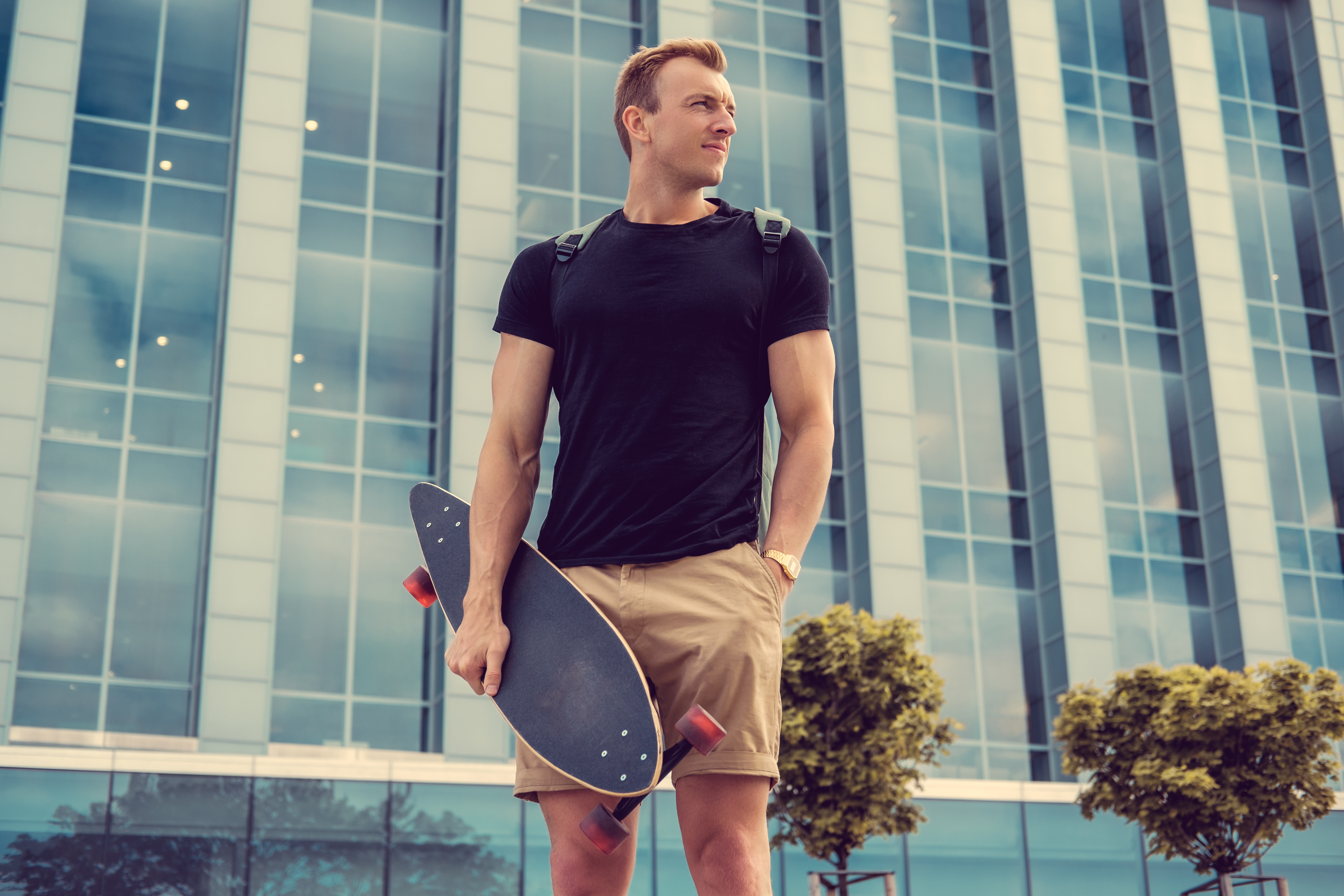 casual-urban-male-holding-longboard-posing-glass-building-background