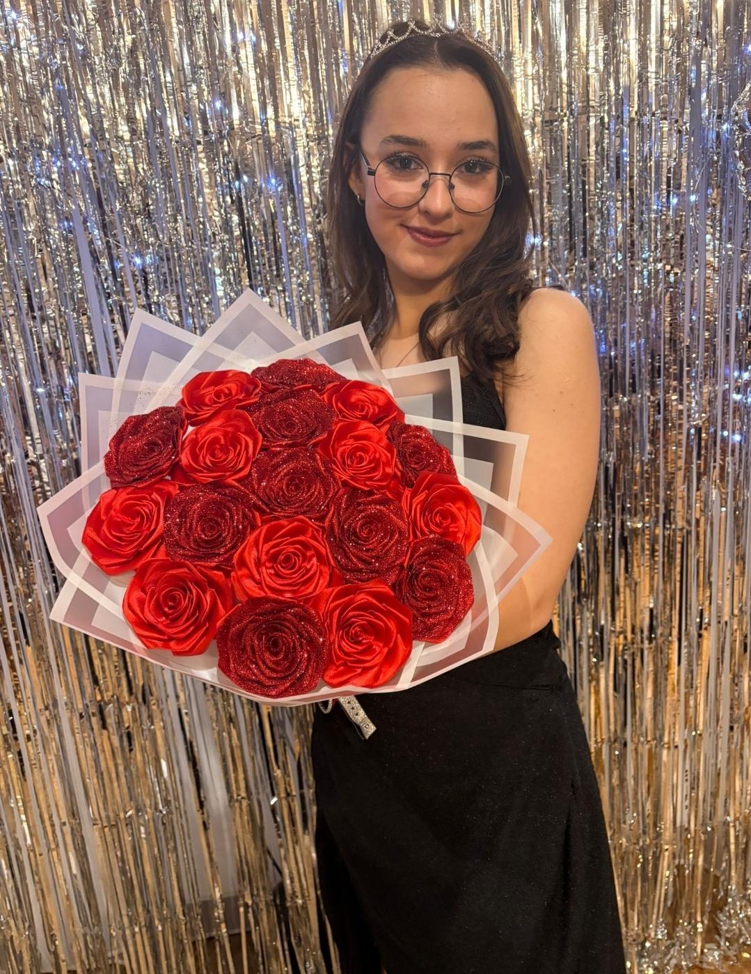 Zářivě červená kytice ze stuh v dárkovém balení držená v rukou oslavenkyně