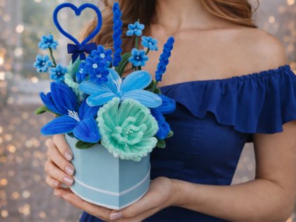 Žena v modrých šatech drží flower box s modrými a mentolovými květy ručně vyrobenými z modelovacích drátků, doplněný modrým srdíčkem.
