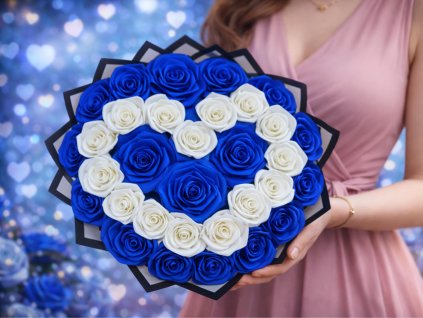 Žena v modrých šatech drží bohatou kytici ze saténových růží, kde bílé růže tvoří tvar srdce uprostřed sytě modrých růží v černém dárkovém papíru.